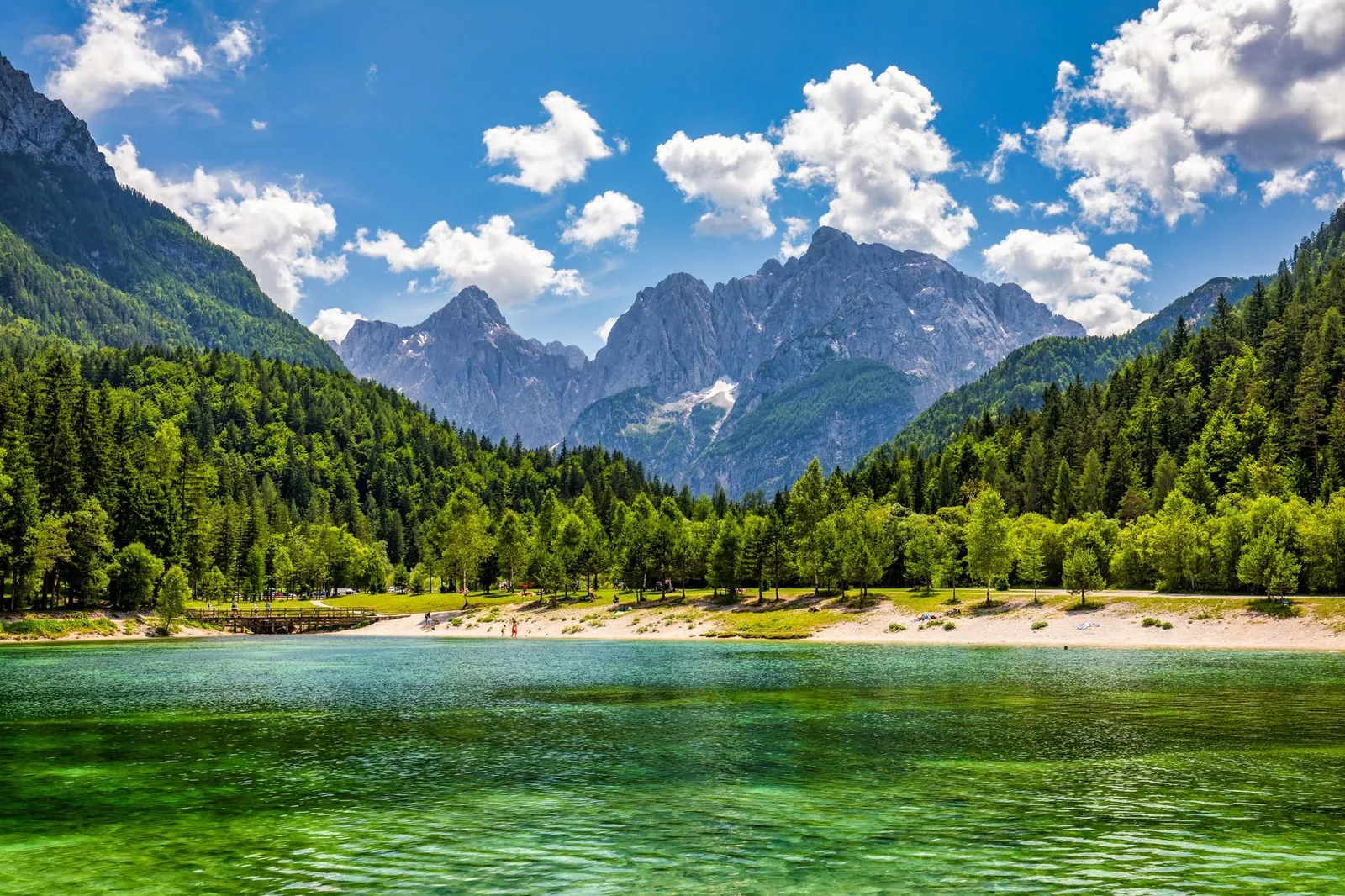 Clear lake water and green woodland beneath the peaks of Slovenia’s Julian Alps